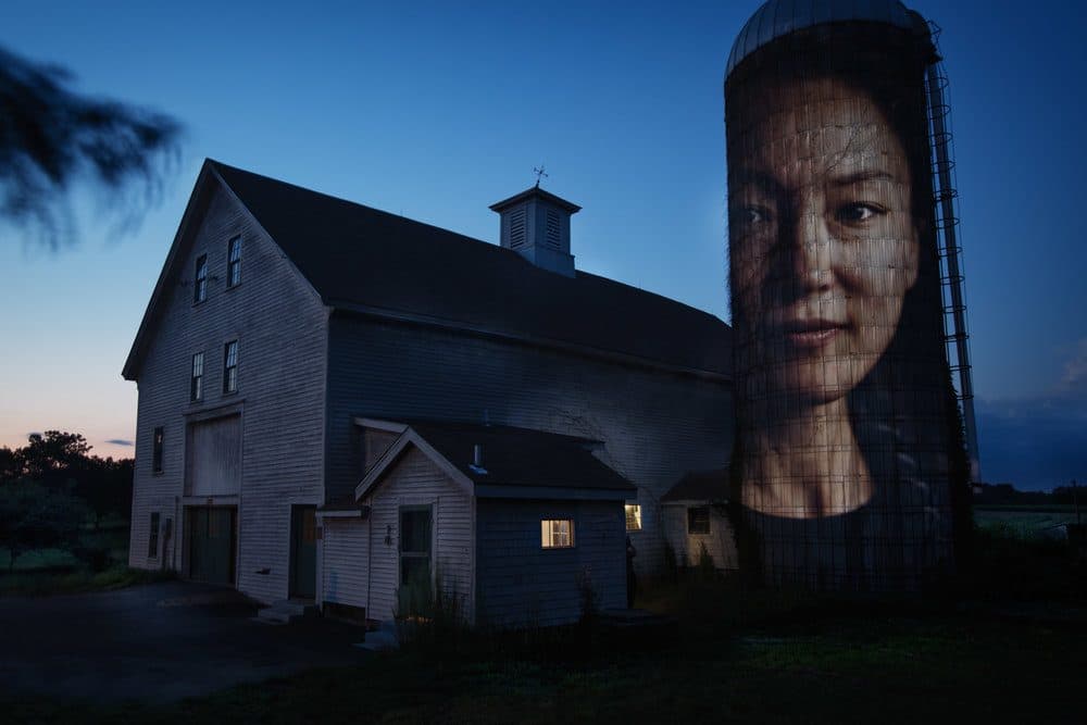 A portrait of Jennifer Hyoje-Ryu Kenty projected onto a barn's silo at Alexander Farm in Winchendon. Originally from South Korea, now works as a researcher at Harvard and an organic farmer. (Courtesy Erik Jacobs)
