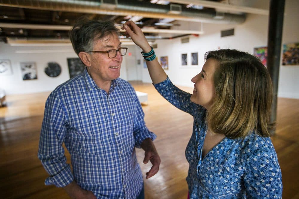Artist Enrique Flores-Galbis laughs as Olivia Ives-Flores fixes her father's hair for a photo opportunity. (Jesse Costa/WBUR)