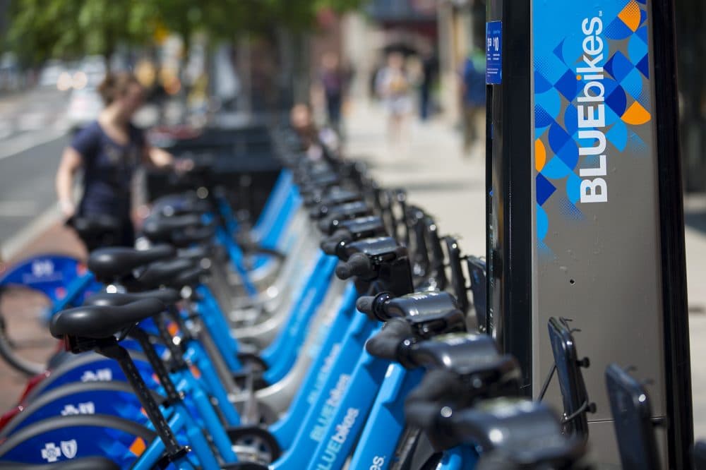 A woman returns a Blue Bike to a station in Kendall Square. (Jesse Costa/WBUR)