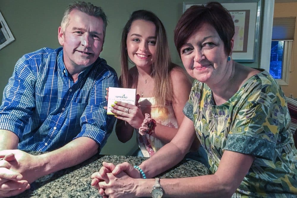 Grace O'Leary, 16, holds a box of Symdeko, which costs $290,000 per year to treat her cystic fibrosis. She's with her parents, Timothy and Lillian. (Bruce Gellerman/WBUR)