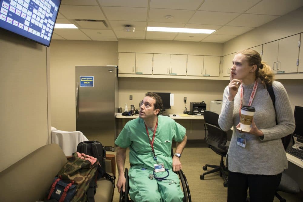 Having returned to work less than a year after being paralyzed from a mountain biking accident, Dr. Daniel Grossman checks the intake status on an electronic board at Saint Marys Hospital emergency room. At right is fellow ER physician Dr. Laura Walker. (Jerry Olson for Here &amp; Now)