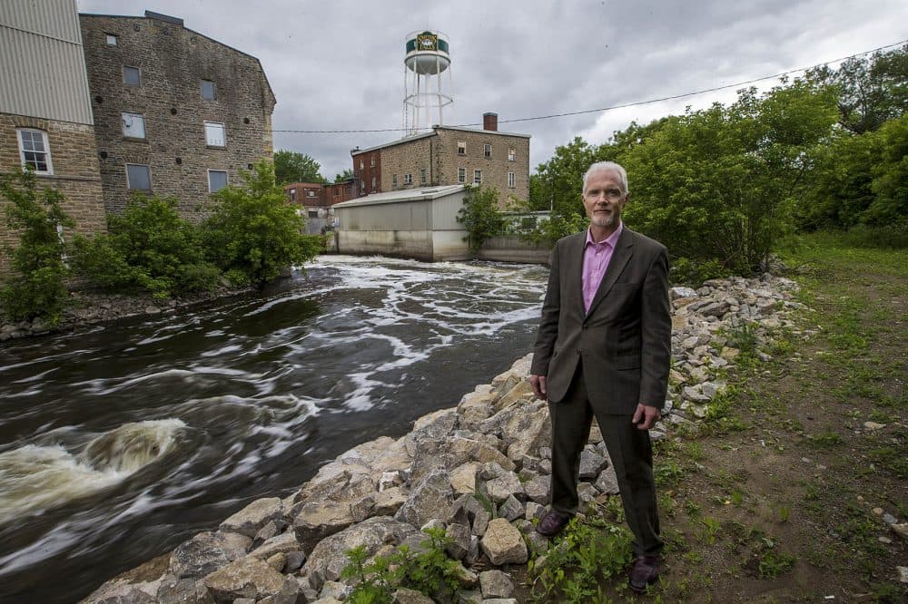 Mayor of Smiths Falls Shawn Pankow stands by the Rideau Canal where the old water treatment facility, left, will be converted into a hotel and hospitality center proposed by the Canopy Growth Corporation. (Jesse Costa/WBUR)