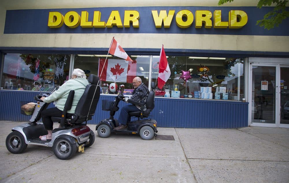 A patriotic elderly couple on scooters rides past the Dollar World store in downtown Smiths Falls. (Jesse Costa/WBUR)