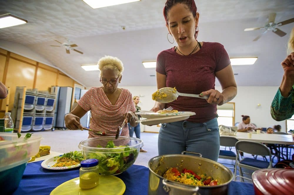 Genie Garda, right, and Amada Gregory grab food at the potluck in Dracut. Gregory is a family advocate at Lowell Alliance. Garda relocated from Puerto Rico after Maria. (Jesse Costa/WBUR)