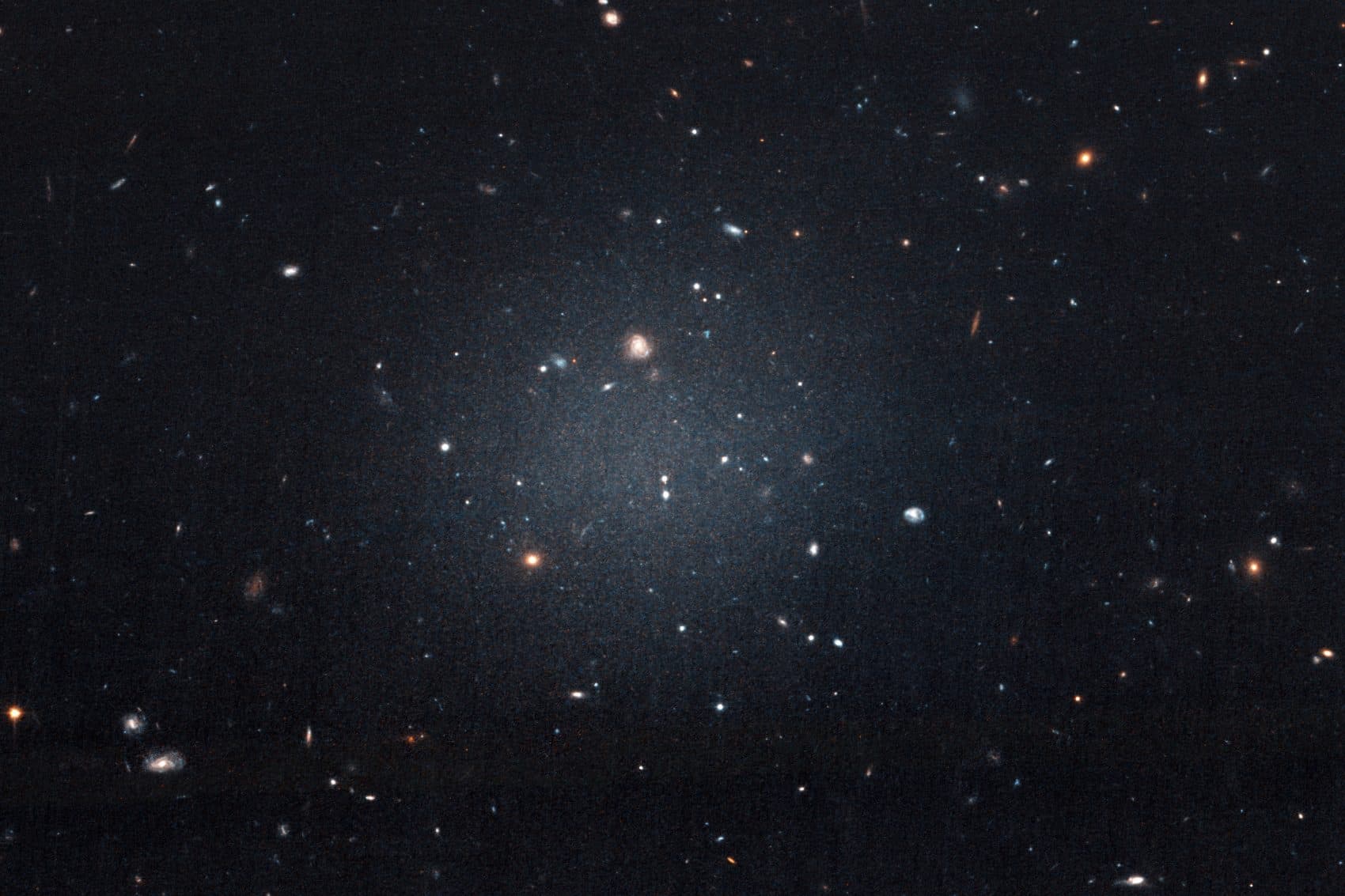 This Nov. 16, 2017 image made with the Hubble Space Telescope shows the diffuse galaxy NGC 1052-DF2, lighter area in center. Several other galaxies can be seen through it. The unusual galaxy’s stars are speeding around with no apparent influence from dark matter, according to a study published on Wednesday, March 28, 2018 in the journal Nature. (P van Dokkum/NASA/ESA via AP)