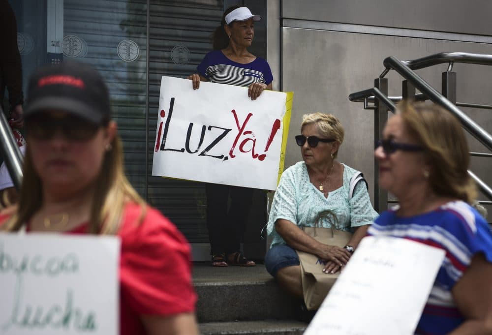 In this May 15, 2018 photo, residents from Yabucoa, where many are still without power, protest outside the Electric Power Authority office, demanding the reestablishment of electricity eight months after Hurricane Maria, in San Juan, Puerto Rico. The sign reads in Spanish &quot;Light now!&quot; (Carlos Giusti/AP)