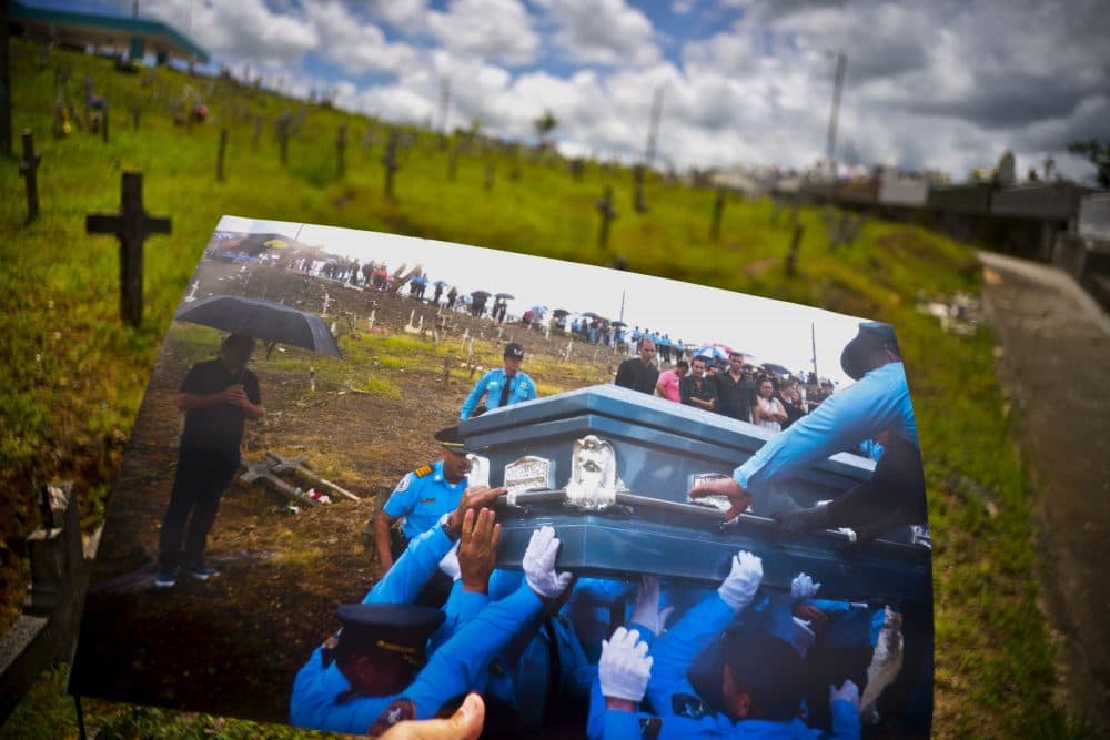 A printed photo taken on Sept. 29, 2017 showing police lifting the coffin of officer Luis Angel Gonzalez Lorenzo, who was killed during the passage of Hurricane Maria when he tried to cross a river in his car, is shown at the same cemetery in Aguada, Puerto Rico, May 31, 2018. The local police force of Aguadilla and Aguada lacks about a dozen officers since the storm, due to resignations and retirements. The U.S. territory's bankruptcy has frozen promotions, salaries, new hires and some police academies have even closed. (Ramon Espinosa/AP)