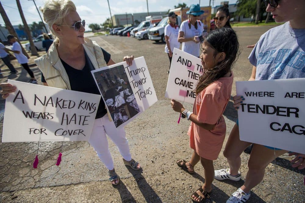 Loren Kruger hands out a protest sign to protest the treatment of immigrant families crossing the U.S. border from Mexico illegally. (Jesse Costa/WBUR)