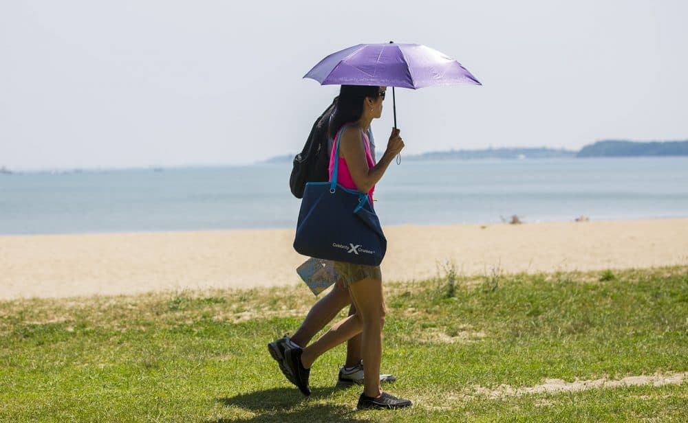 To keep out of the hot sun, a couple walks along the the edge of the grass along Carson Beach in South Boston in the 90 degree weather. (Jesse Costa/WBUR)