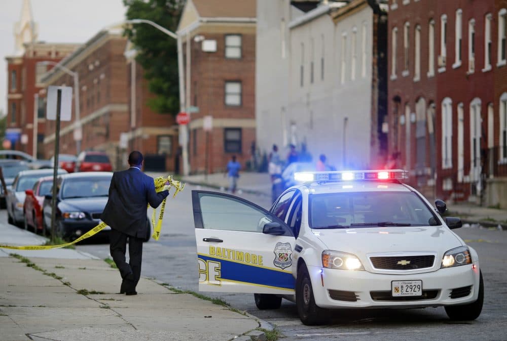In this July 30, 2015 picture, a member of the Baltimore Police Department removes crime scene tape from a corner where a victim of a shooting was discovered in Baltimore. (Patrick Semansky/AP)