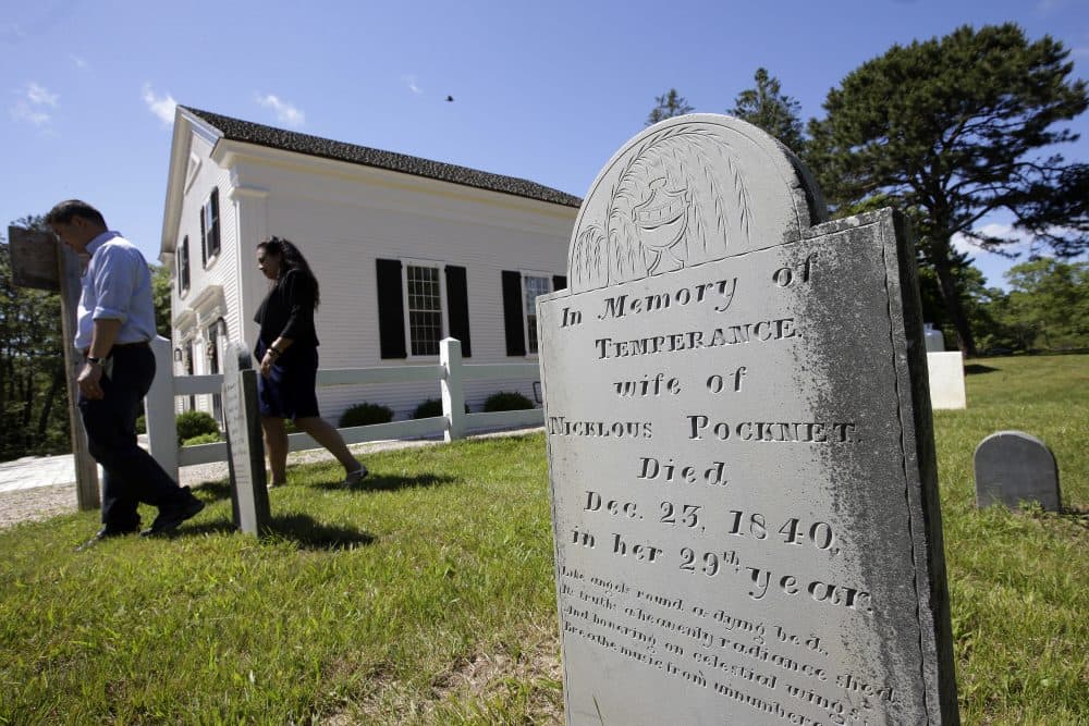 A gravestone dated 1840 stands near the Mashpee Old Indian Meeting House, behind, on Mashpee Wampanoag tribal land, on Cape Cod. The tribe says an unfavorable decision from the U.S. Interior Department on its tribal reservation status would effectively shut down certain government operations, including the tribe's new court system and police force. (Steven Senne/AP)