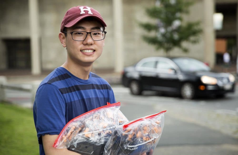 Sophomore Raymond So holds bags of ear plugs and sleep masks for distribution to Harvard freshmen. (Robin Lubbock/WBUR)