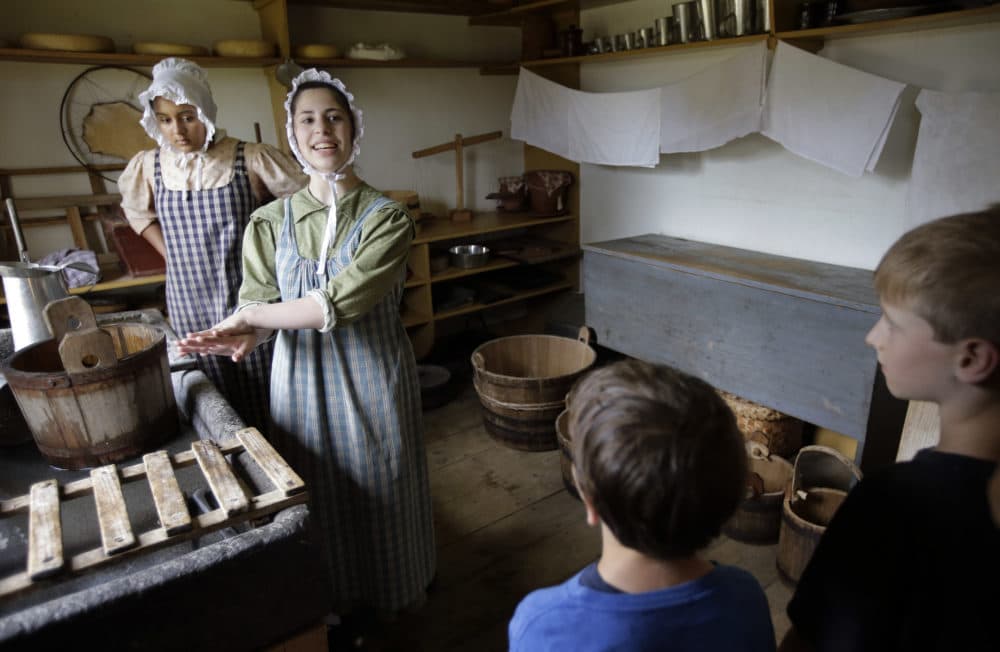 Hannah Ingersoll, left, and Loralei Arndt, second from left, reenact 1830s farm workers as children look on in a cheese room at Old Sturbridge Village. (Steven Senne/AP)