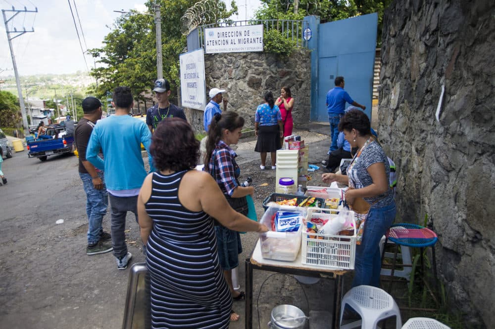 Poco después de ser liberados, los deportados le compran refrigerios y otras cosas a una mujer que se encuentra fuera del Centro de Atención Integral al Migrante en San Salvador. (Jesse Costa/WBUR)