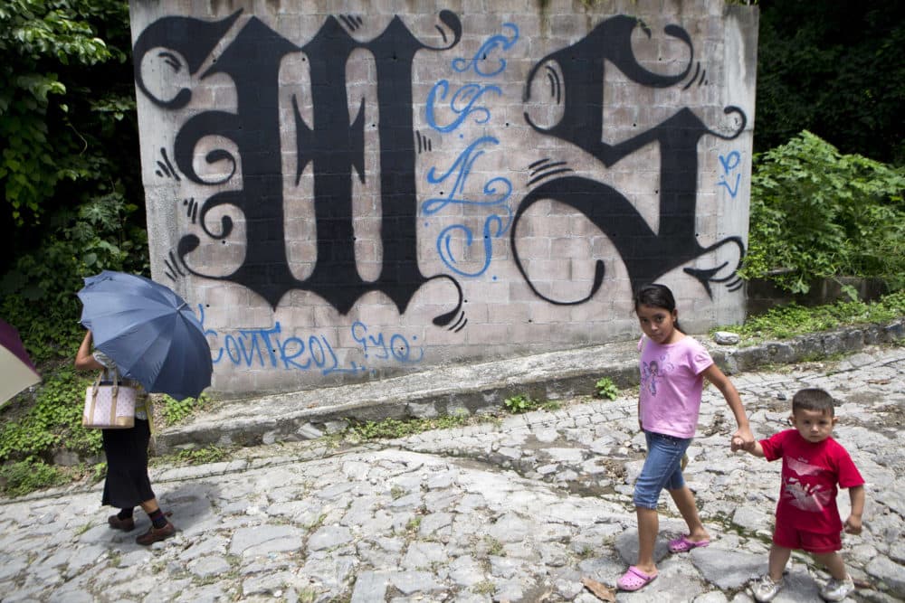 In this Aug. 21, 2014 file photo, a family walks by a wall covered by a symbol from the Mara Salvatrucha, of MS-13 gang in Ilopango, El Salvador. (Esteban Felix/AP)