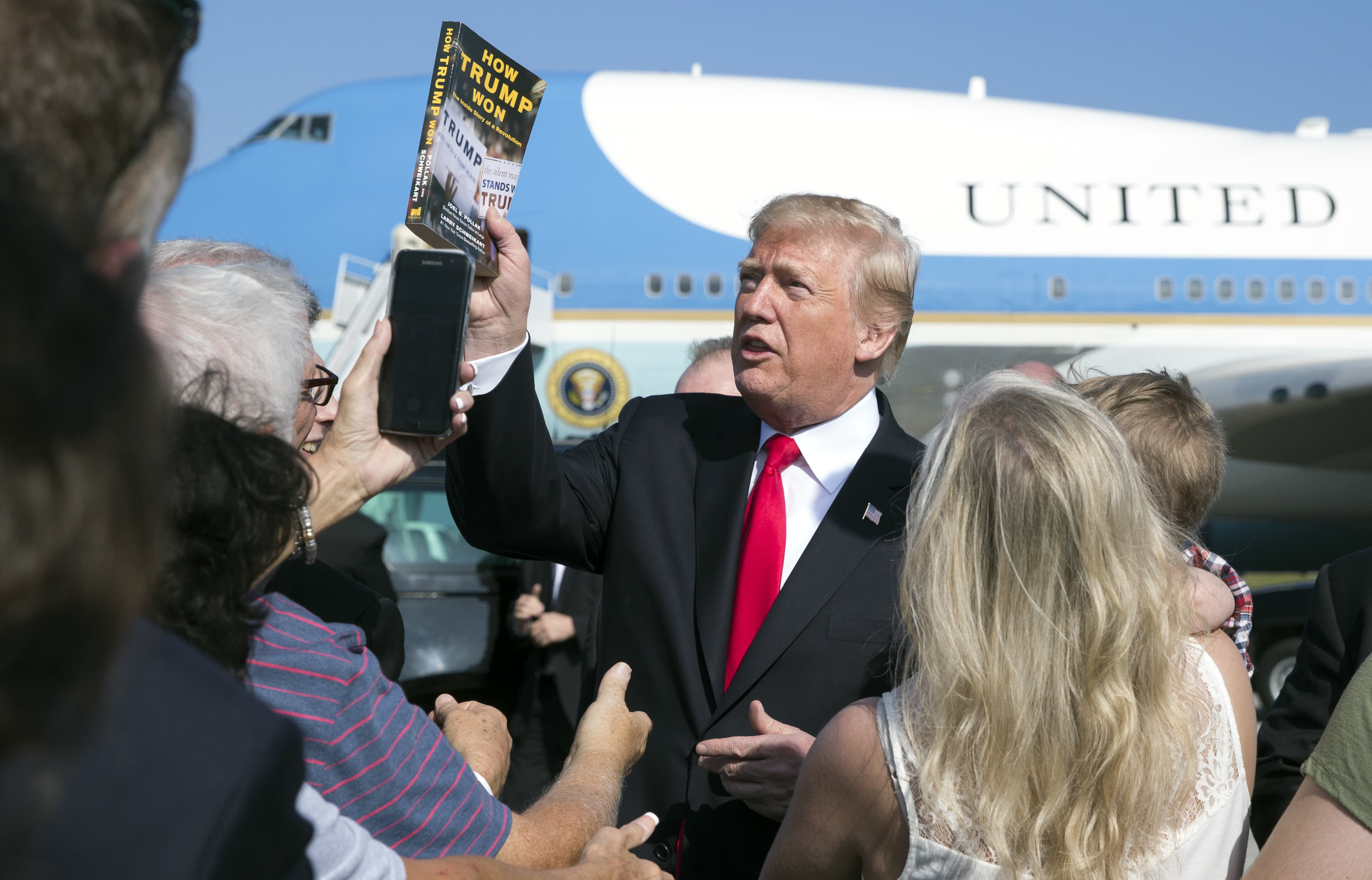 President Donald Trump holds up the book "How Trump Won The Inside Story of a Revolution" as he greets people on the tarmac as he arrives on Air Force One at Palm Beach International Airport, in West Palm Beach, Fla., Friday, Dec. 22, 2017. (Carolyn Kaster/AP)