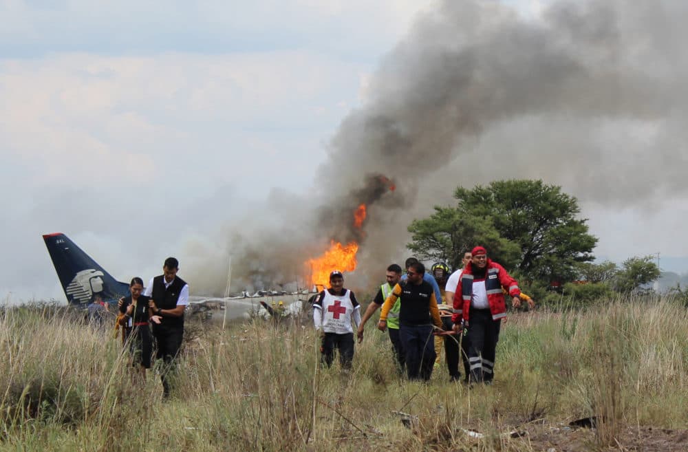Red Cross and rescue workers carry an injured person on a stretcher, as airline workers walk away from the site where an Aeromexico airliner crashed in a field near the airport in Durango, Mexico July 31, 2018. (Red Cross Durango via AP)