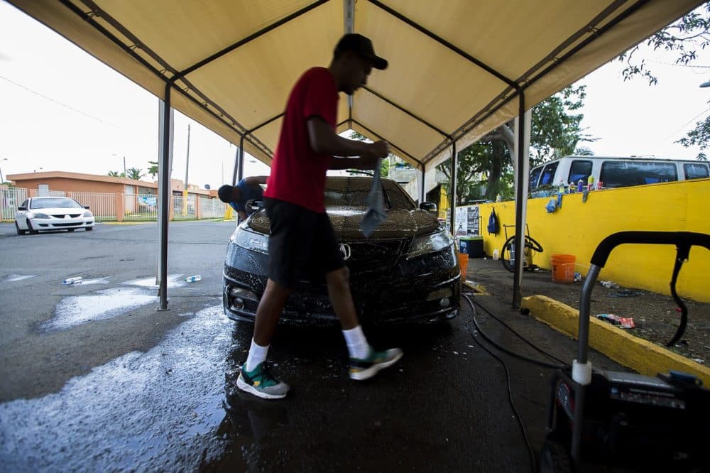 A worker at a pop-up car wash in Bravos de Boston walks around a car he is cleaning. Unemployment remains high on the island and many are doing everything they can to make ends meet. (Jesse Costa/WBUR)