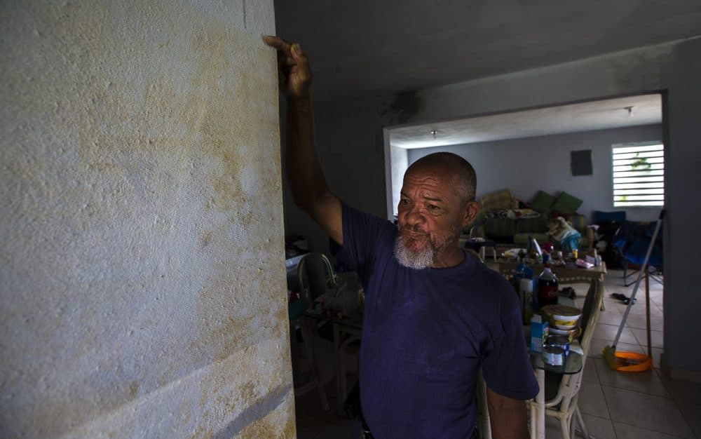 Jose Cruz points to a water line showing how high floodwaters from a canal running along Calle Progreso had risen in his house during Hurricane Maria. He fled to another location during the storm, but he is now building a second floor onto his house, for when the next severe storm causes flooding. (Jesse Costa/WBUR)