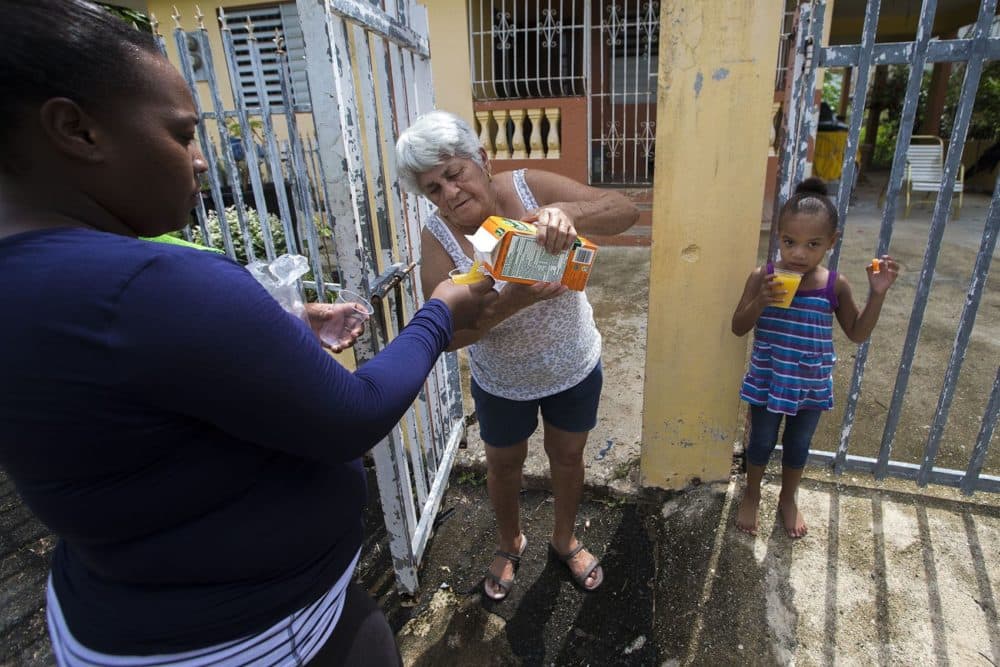 Juana Alicea pours cups of orange juice to Indiana Medina and 3-year-old Kendra as they were walking past her house on a hot day in Toa Baja. (Jesse Costa/WBUR)
