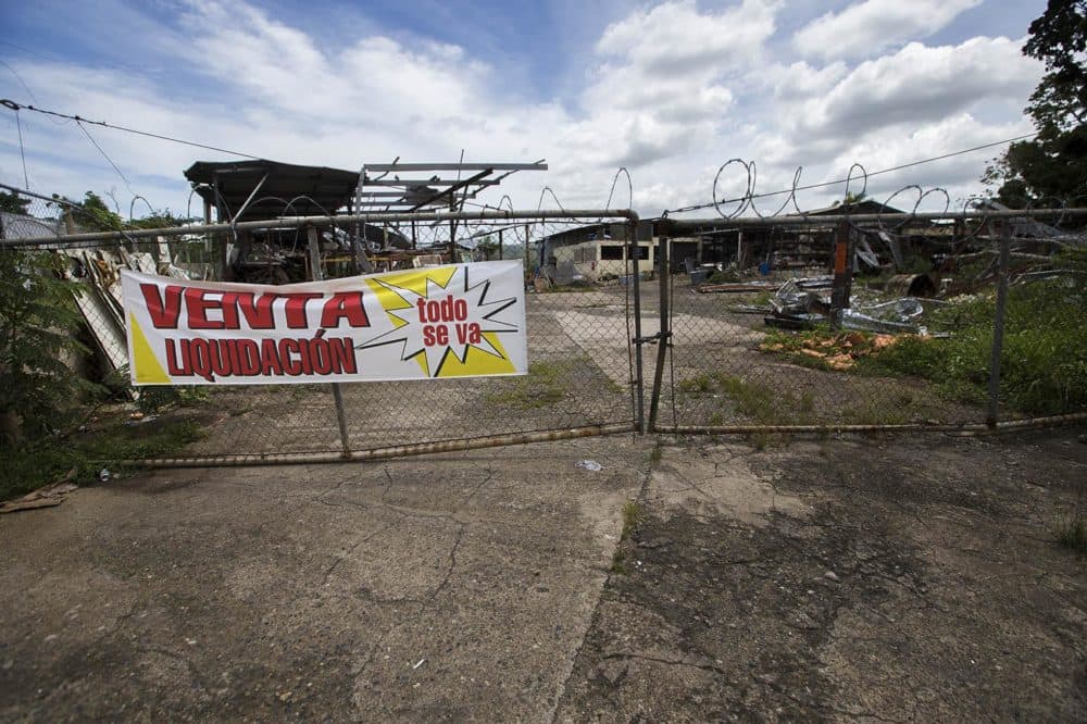 We return to the lumberyard owned by Ivonne Beltran's family in Corozal that was destroyed by Hurricane Maria. A year later, a sign on the fence announces a liquidation sale. (Jesse Costa/WBUR)