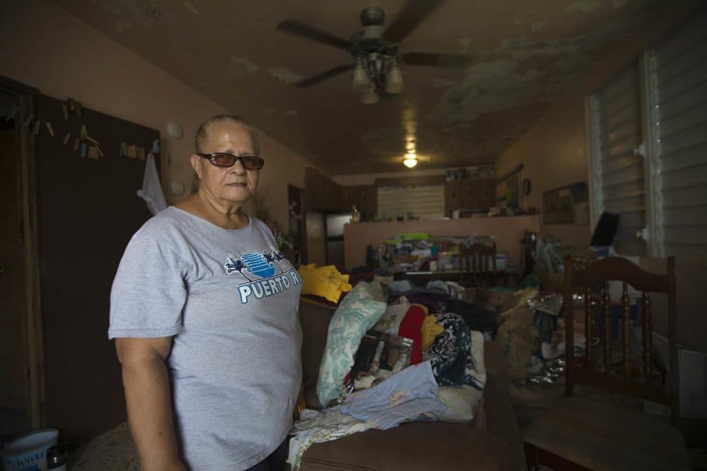 Ada Alvarez Córdova stands in her house in Guaynabo, where her belonging are piled into the center of rooms since water leaks in around perimeter walls. The roof and ceiling sustained damage during Maria and she says FEMA has rejected claims for assistance, despite never assessing the damage. (Jesse Costa/WBUR)