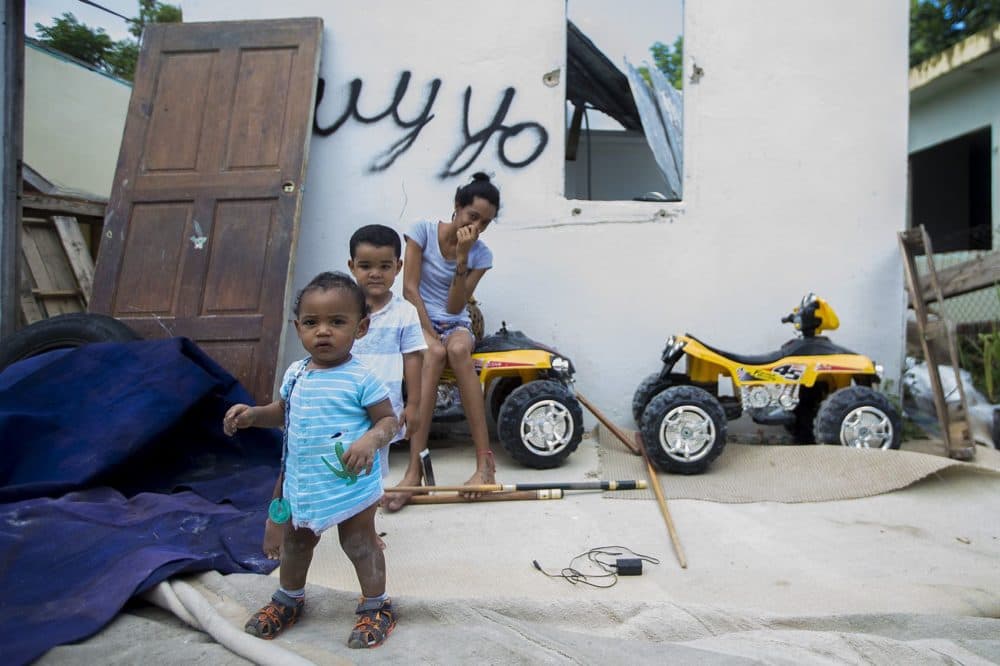 A mother and her two children are in front of a house destroyed by Maria on Calle 13 in Barrio Obrero, San Juan. Many residents on this street were relocated by the government and the houses left abandoned. (Jesse Costa/WBUR)