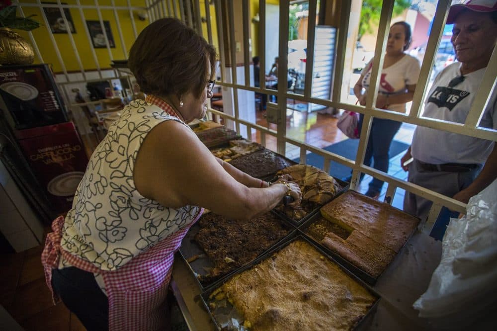 Behind a cage, Isabel Quintanilla prepares to slice on of the breads she offers to customers at her bakery Panaderia Pacita Quintanilla in San Vicente, El Salvador. She fears retaliation from local gangs that have tried extorting money from her before. (Jesse Costa/WBUR)