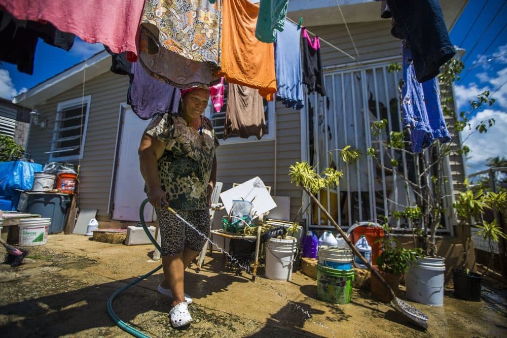 Angelina Arroyo sprays her driveway down during a hot afternoon in Punta Santiago. Her husband had a heart attack shortly after the hurricane last year and died soon after. (Jesse Costa/WBUR)