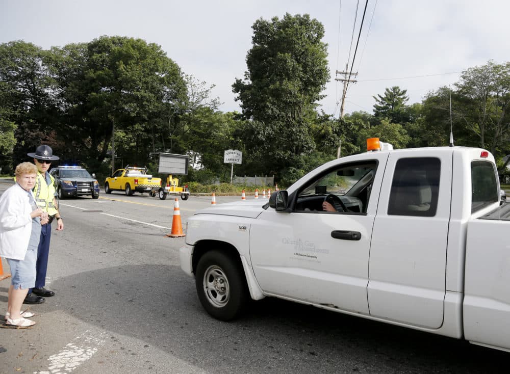 A Columbia Gas truck passes through a roadblock as a member of the state police talks to a pedestrian on Route 114 in North Andover at the Lawrence city line (Mary Schwalm/AP)