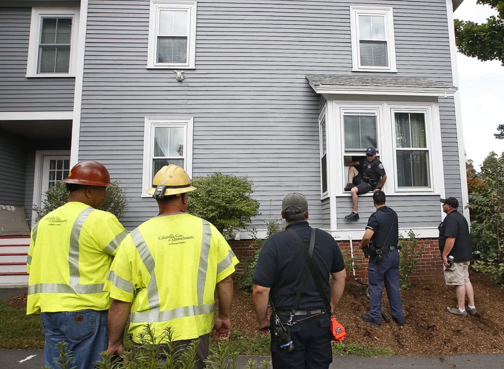 As Columbia Gas employees look on, an Andover police officer comes out the window of an evacuated house after checking that there is no presence of gas and that the gas in the house is turned off Friday in Andover. (Winslow Townson/AP)