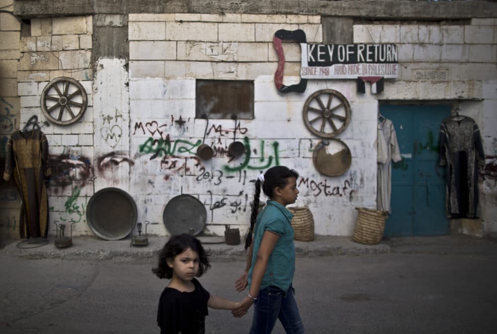 Palestinian sisters hold hands as they walk past a wall decorated with traditional dresses and other items, on display outside a souvenir shop, in the West Bank refugee camp of Aida, Bethlehem, Tuesday, June 24, 2014. (Muhammed Muheisen/AP)
