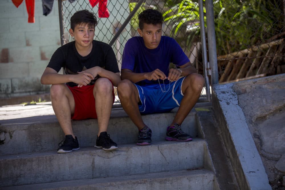 Two Salvadoran teenaged boys sit on steps in the shade while taking a break from playing soccer at a field in the community of Las Palmas in San Salvador. (Jesse Costa/WBUR)