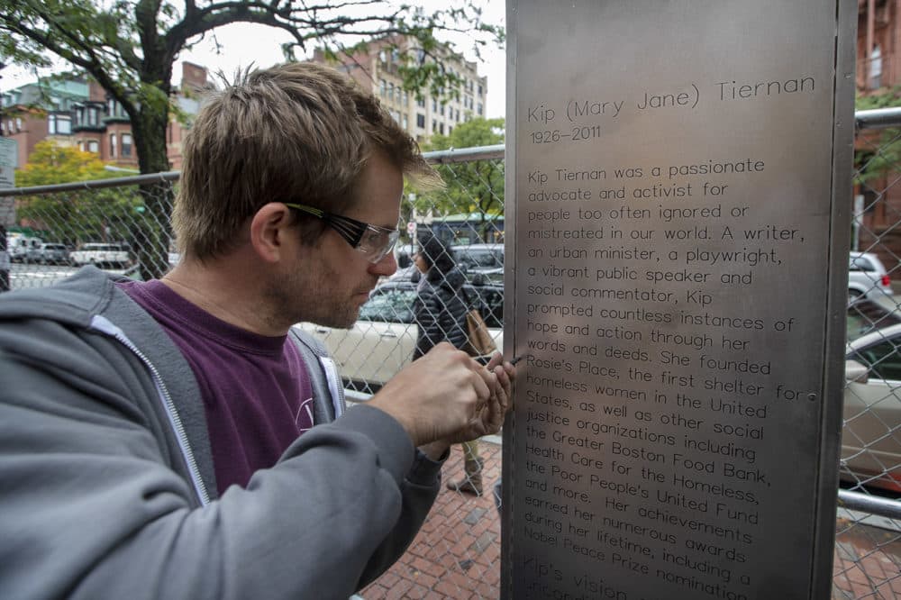 Jackson Morley fastens a panel with Kip Tiernan’s biography on it into place on the memorial honoring her being built on Dartmouth Street. (Jesse Costa/WBUR)