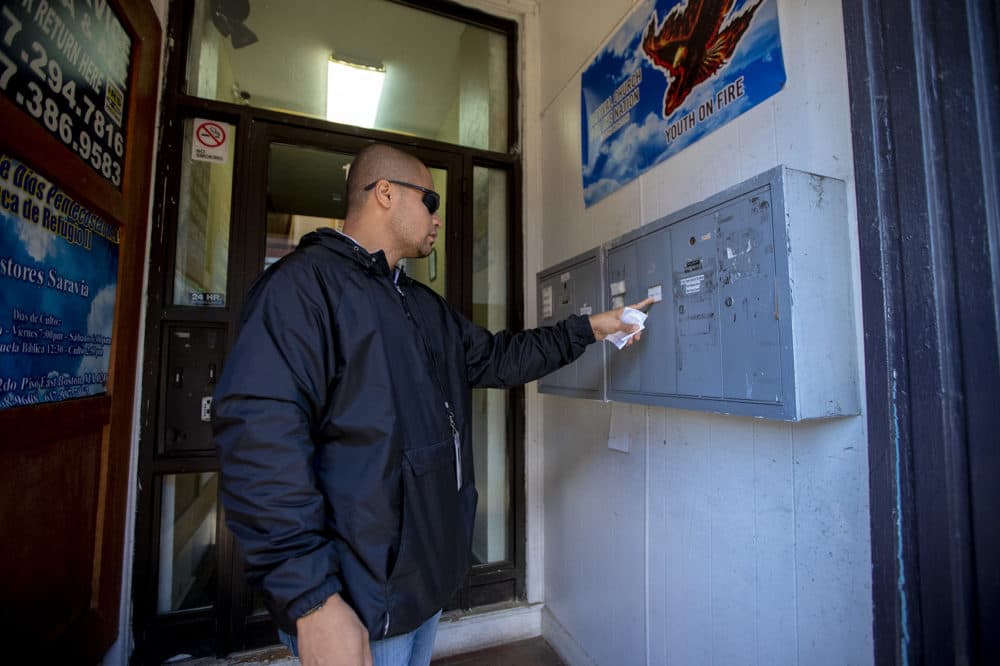 Diego Pizarro looks at mailboxes at a East Boston apartment building, only to find out all the occupants of the building are all businesses. (Jesse Costa/WBUR)