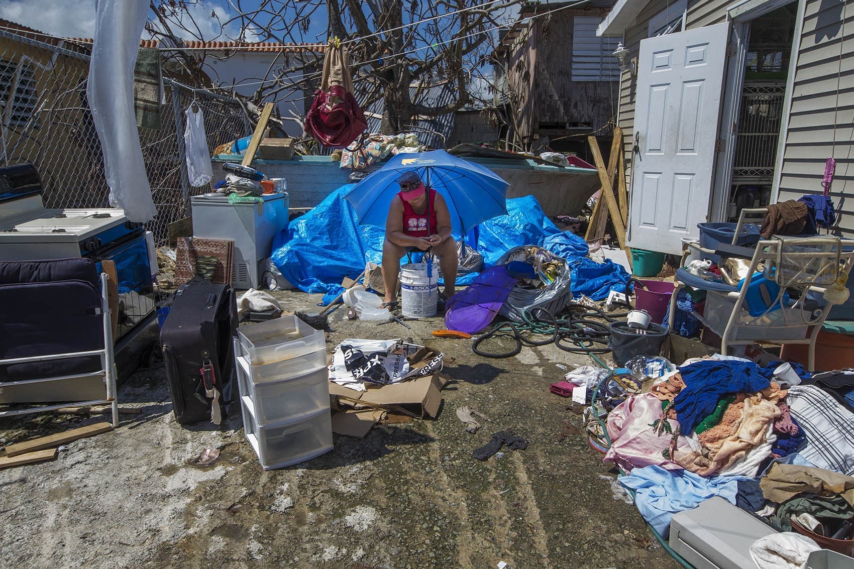 In this 2017 photo, Punta Santiago resident Angelina Arroyo Rivera cleans knives and plastic containers under an umbrella to shield her from the hot sun. (Jesse Costa/WBUR)