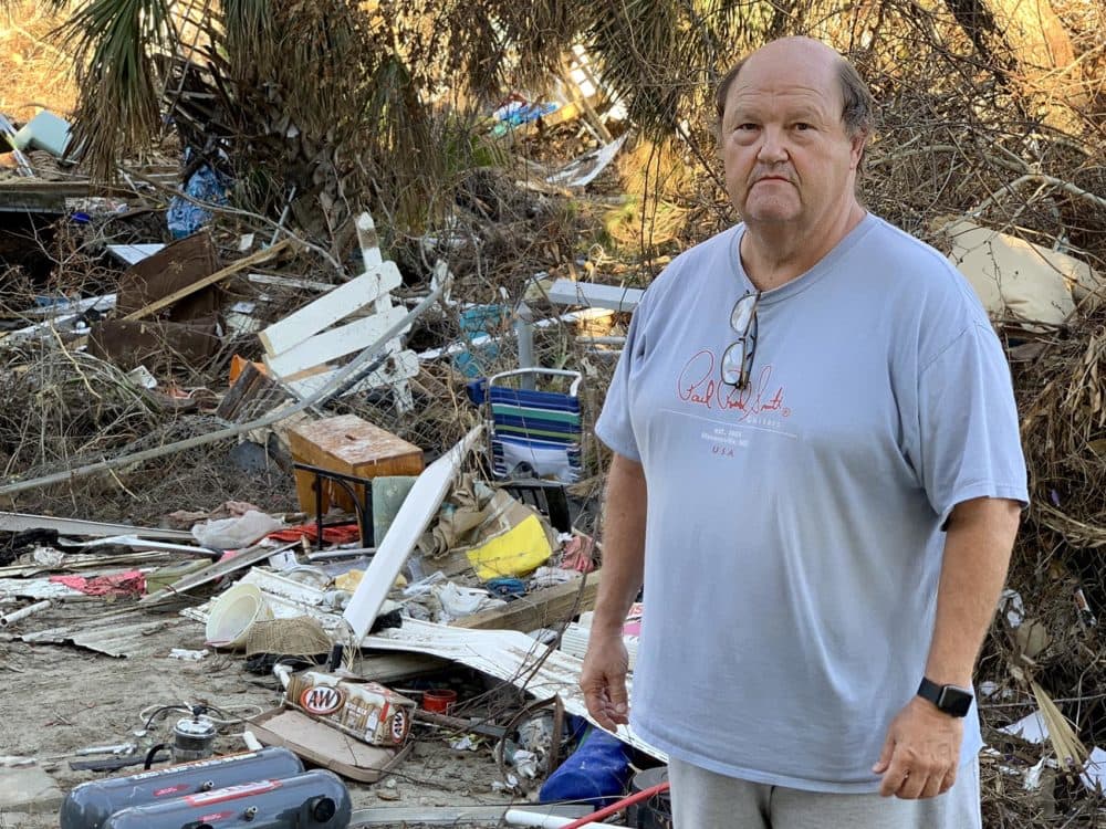 Troy Bryant in his backyard, with pieces of white picket fence strewn about among debris from his house and his neighbors'. (Chris Bentley/Here &amp; Now)