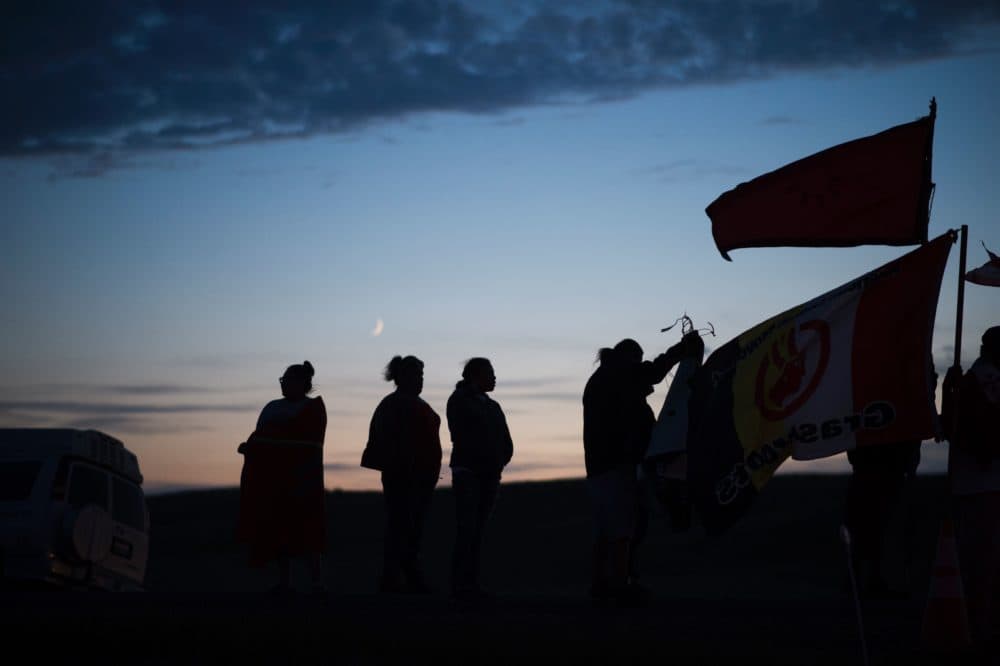 People stand with flags against the backdrop a crescent moon after sunset at an encampment for people joining the Standing Rock Sioux Tribe's protest against the construction of the Dakota Access Pipeline (DAPL), near Cannon Ball, N.D., on Sept. 3, 2016. (Robyn Beck/AFP/Getty Images)