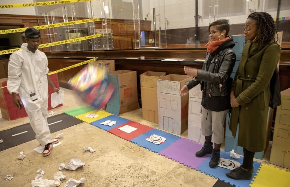 Veronica Wells (with reporter Jacquinn Sinclair alongside her) throws the dice to see how far she can get around the board. &quot;I felt the game was rigged,&quot; she says after playing the game. &quot;I've felt that in real life.&quot; (Robin Lubbock/WBUR)