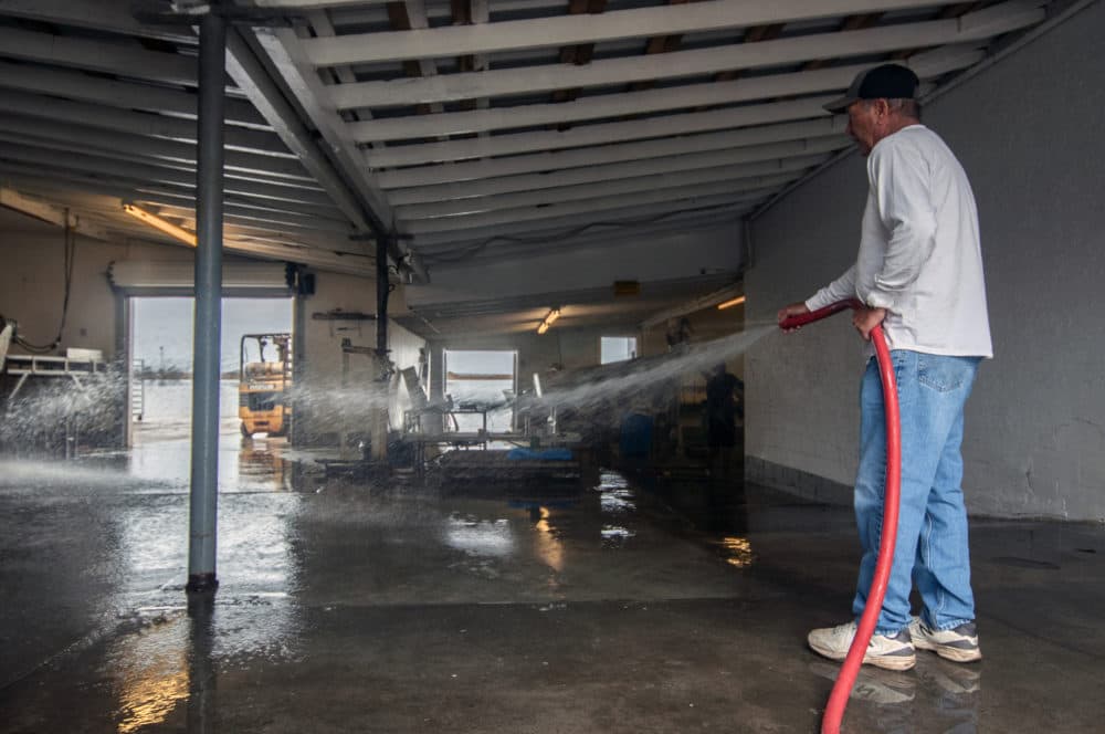 Walter Ward, co-owner of 13 Mile Seafood, washes away muck and debris from his oyster processing facility in Apalachicola, Fla. (Chris Bentley/Here &amp; Now)