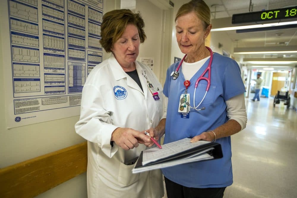Theresa Capodilupo, a nurse director and Brenda Pignone, a bedside nurse, review the daily patient assignment sheet for a post-surgery and trauma unit at Massachusetts General Hospital. They, like other nurses in the state, are watching Question 1 closely. (Jesse Costa/WBUR)