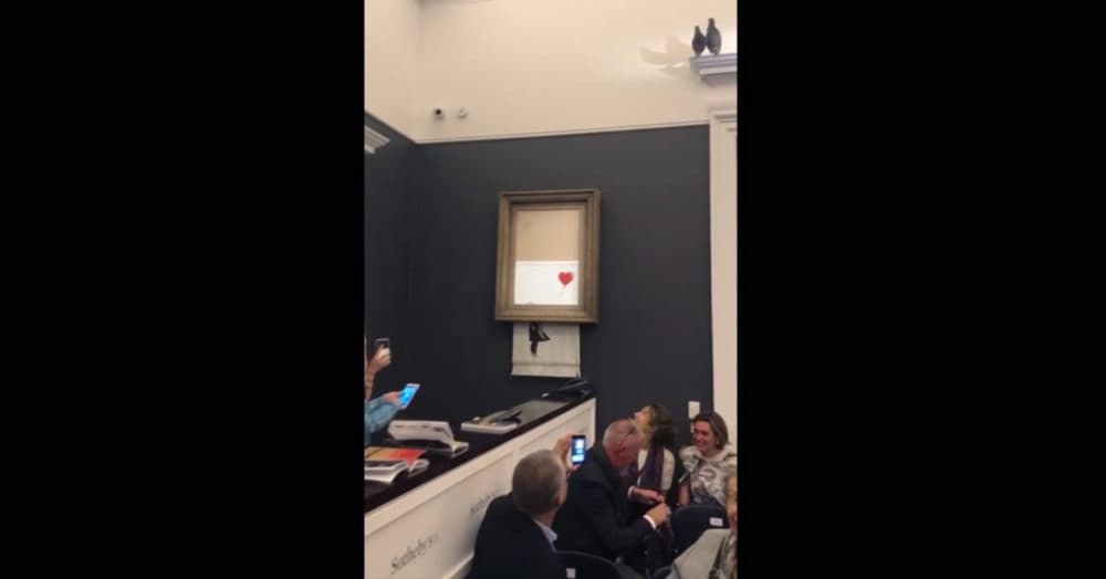 In this grab taken from video on Friday, Oct. 5, 2018, people watch as the spray-painted canvas "Girl with Balloon" by artist Banksy is shredded at Sotheby's, in London. (Pierre Koukjian/AP)