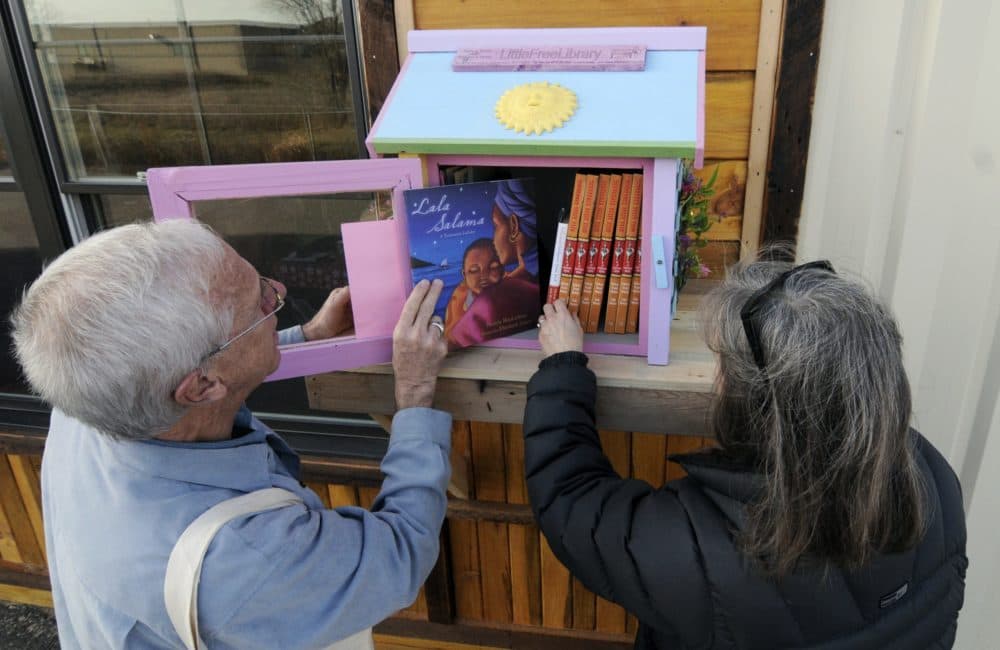 In this 2012 photo, Rick Brooks, left, looks through the small glass door as he and Elizabeth Kennedy pose beside one of the Little Free Libraries lending boxes, in Hudson, Wis. (Jim Mone/AP)