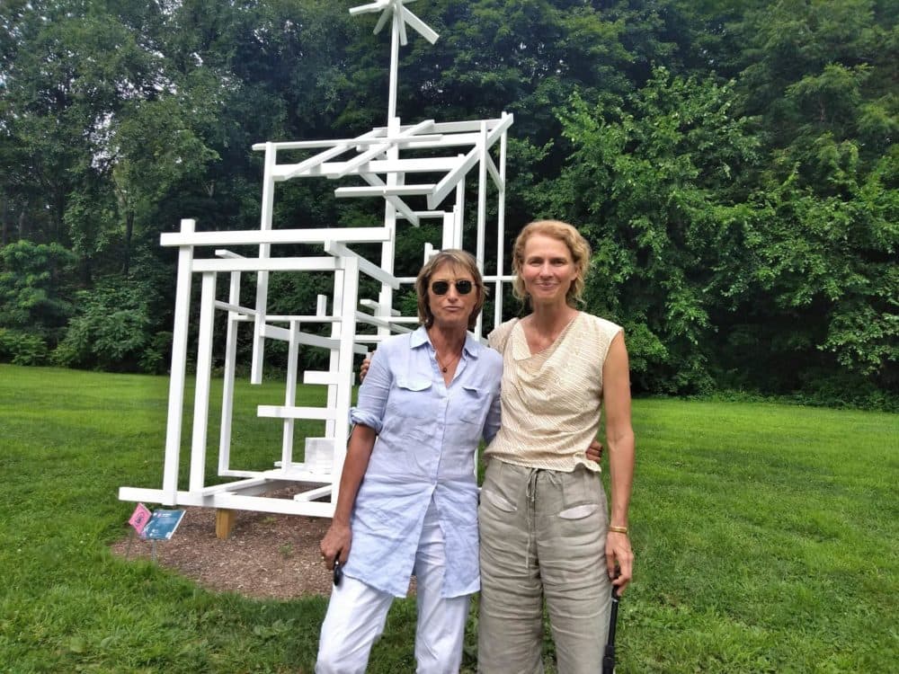 Curators Eva Fierst, left, and Sandy Litchfield stand with &quot;Ghost Shed&quot; by Tom Friedman. The sculpture is installed on land that used to be occupied by frat houses. (Jill Kaufman/NEPR)