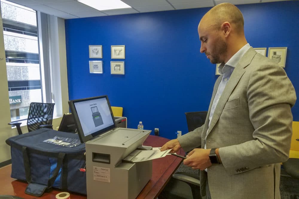 Clear Ballot CEO Jordan Esten places a ballot into the company's voting machine, which scans digital images of ballots and collects the paper copies in a bag. The images are stored on encrypted USB sticks, as the system is offline and has no modem. (Zeninjor Enwemeka/WBUR)