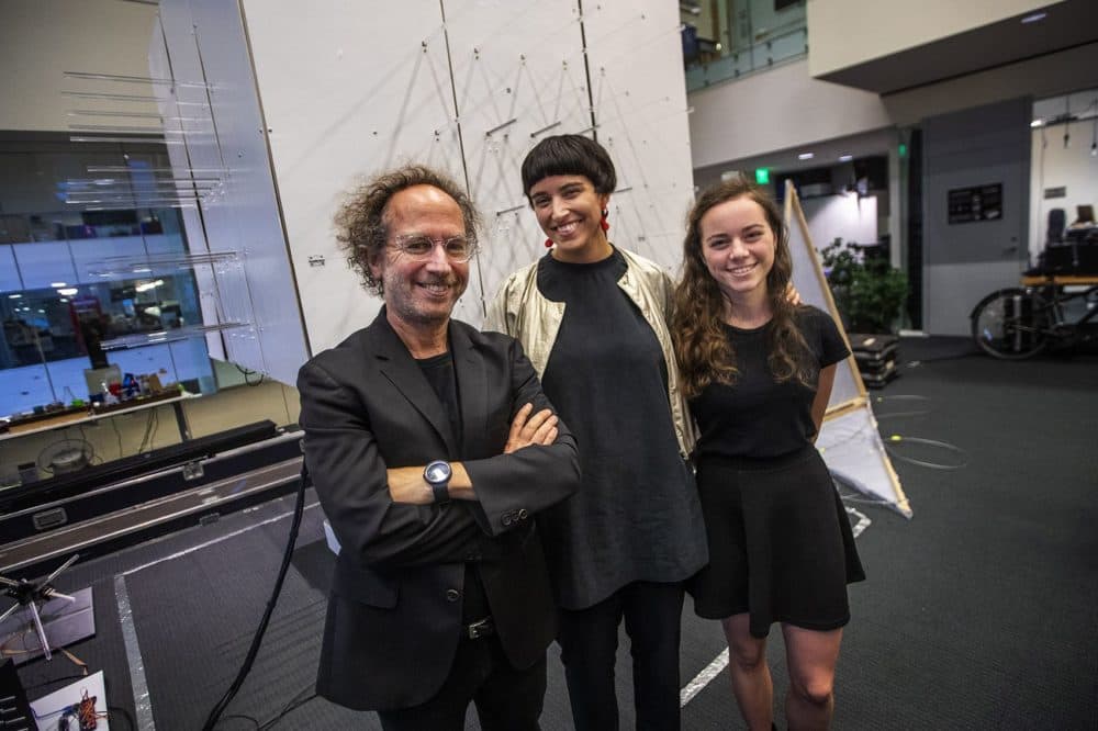 Director of the MIT Media Lab Tod Machover, Nicole L’Huillier and Hannah Lienhart stand in front of &quot;The Cube&quot; a small prototype of a room that changes shape in relation to sound and music being played through it. (Jesse Costa/WBUR)