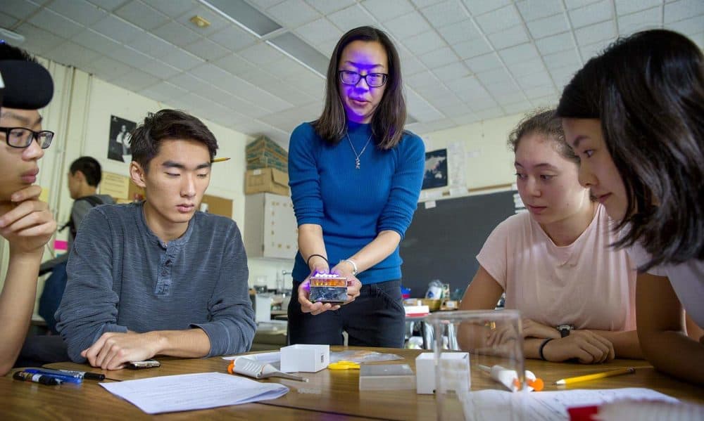 Purple light plays across Ally Huang's face as she lights up a transilluminator to show the results of a BioBits experiment at Brookline High School. (Robin Lubbock/WBUR)