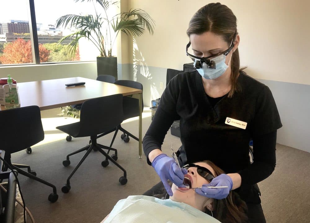 EF employee Maria DeLorenzo gets her teeth cleaned in a conference room at her company’s headquarters. The Massachusetts-based startup Virtudent sets up remote clinics like this one, bringing the hygienist to people who would otherwise be too busy to go to a traditional dentist. (Peter O'Dowd/Here &amp; Now)