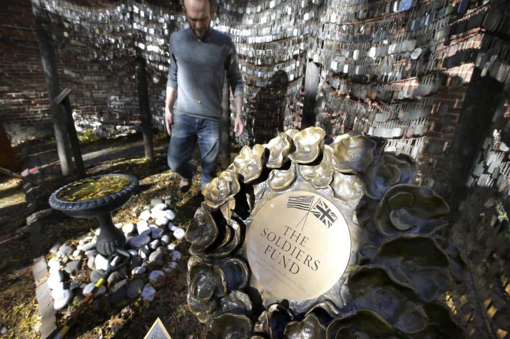In this Wednesday, Nov. 7, 2018 photo Tim Wenrich, of Boston, caretaker at Old North Church, stands near a bronze wreath, right, that is part of a memorial that honors fallen soldiers from the U.S. and Britain, on the grounds of the church in Boston. Since 2005, thousands of military dog tags have hung like wind chimes outside the church in touching tribute to American forces killed in Iraq and Afghanistan. (Steven Senne/AP)