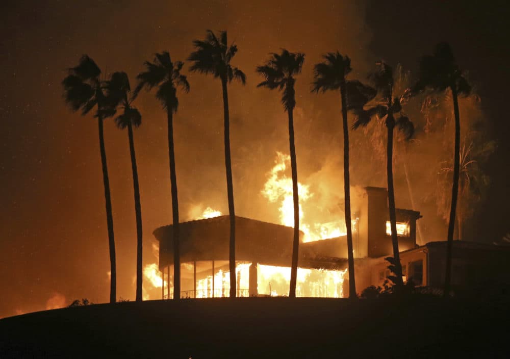 Palm trees frame a home being destroyed by a wildfire above Pacific Coast Highway in Malibu, Calif., Friday, Nov. 9, 2018. Known as the Woolsey Fire, it has consumed tens of thousands of acres and destroyed multiple homes. (Reed Saxon/AP)